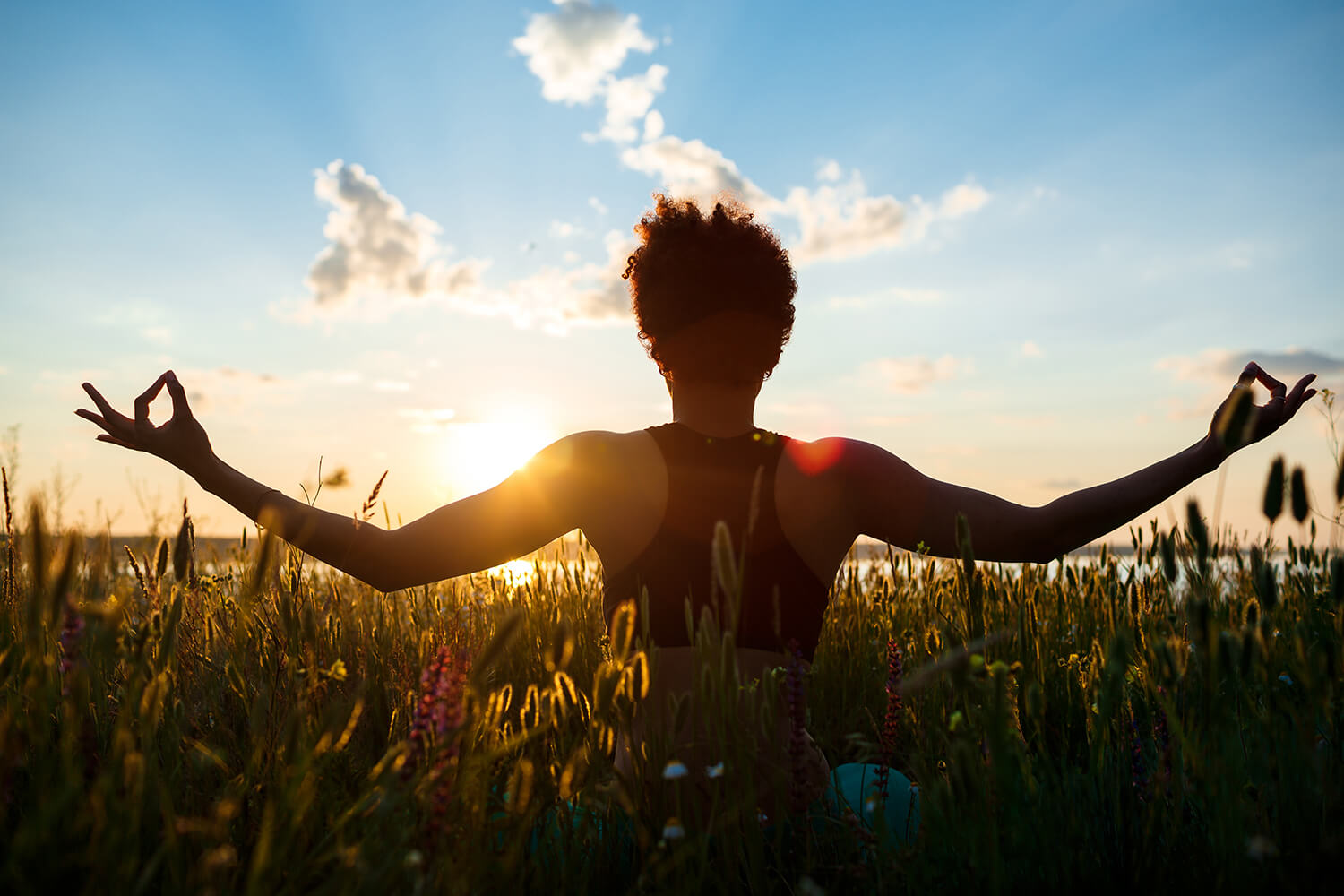 Femme de dos effetuant du yoga dans un champs de blé