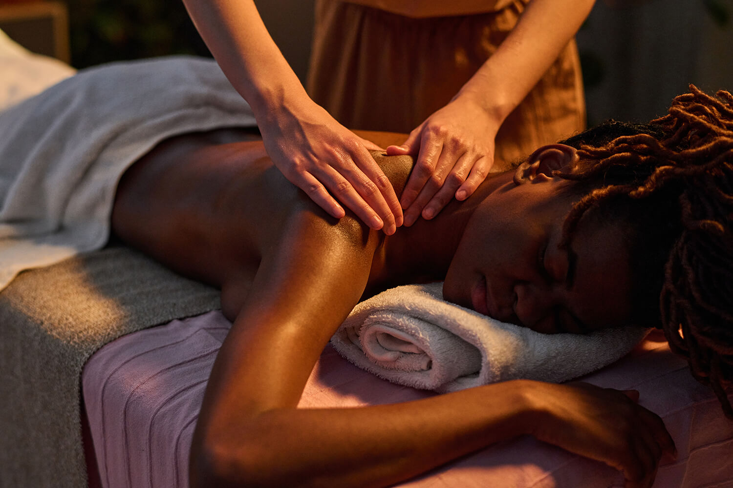 Mains d'un thérapeute massant les épaules d'une femme pour une profonde relaxation musculaire dans une ambiance tamisée