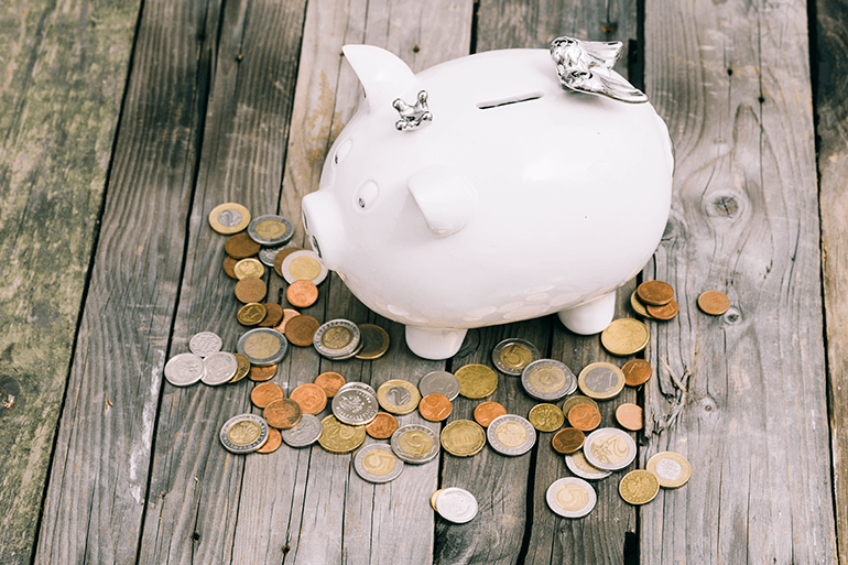 Tirelire en forme de cochon entourée de pièces de monnaie sur une table en bois, illustrant le budget ou les tarifs des soins
